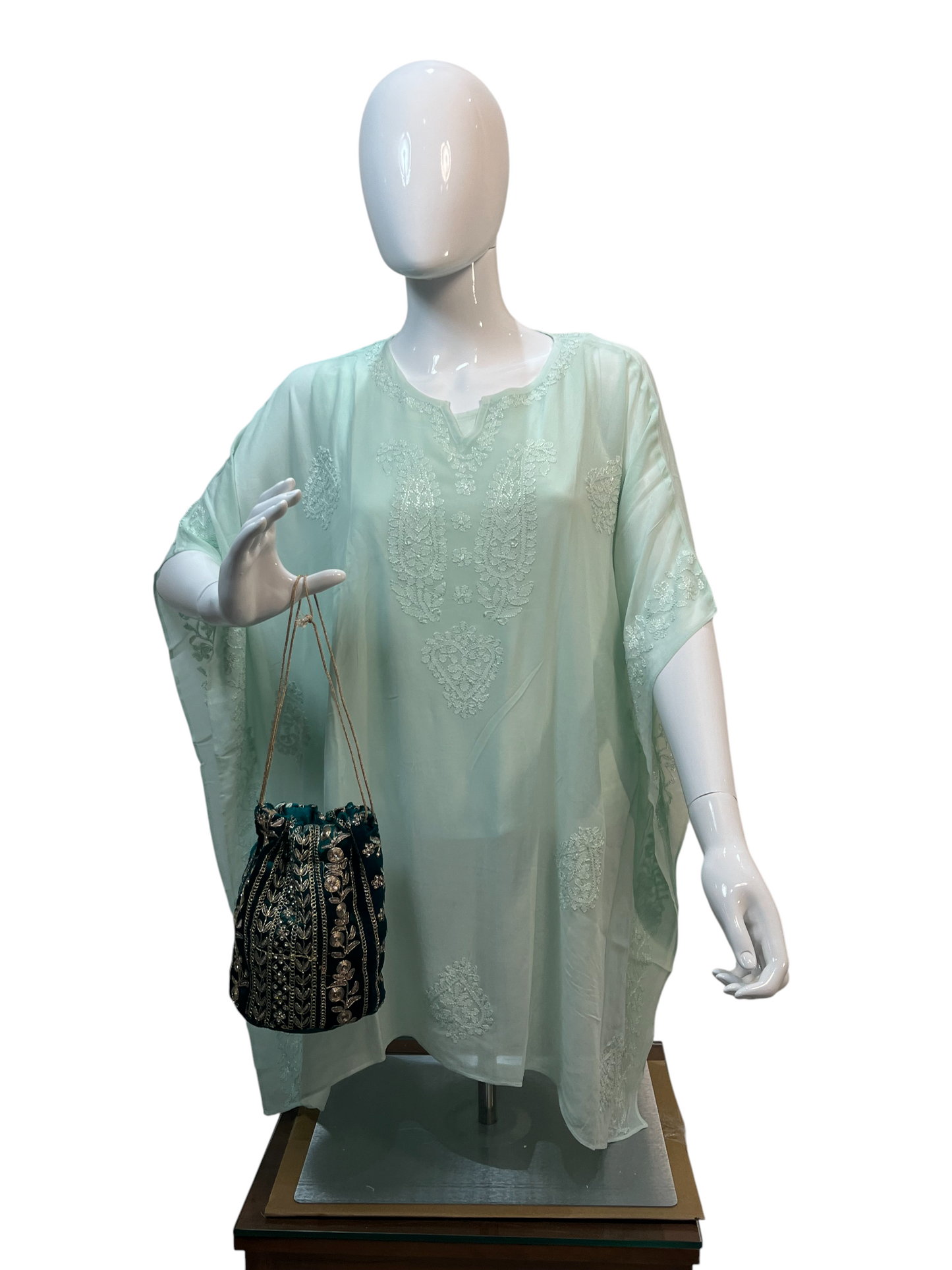 Mannequin wearing a light green embroidered outfit with a black and gold handbag on a white background